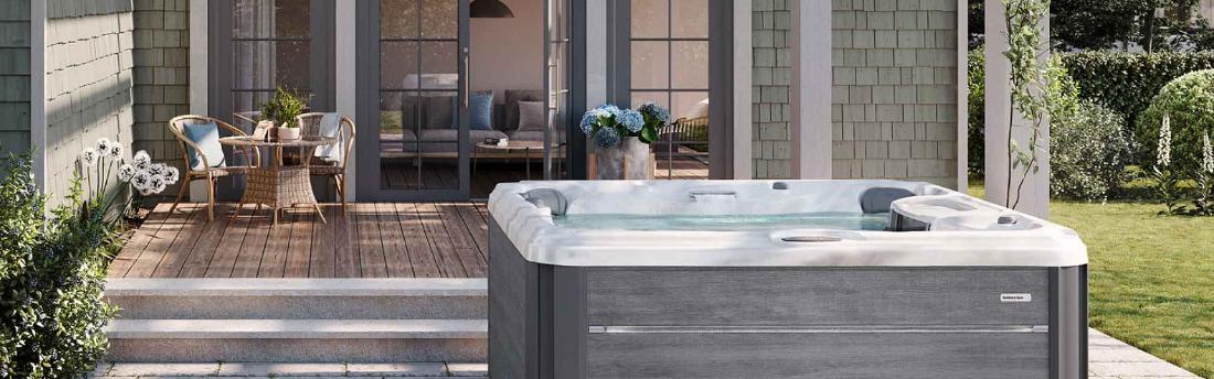 A wide-angle front view of a grey-paneled hot tub on a wooden deck with a waterfall feature