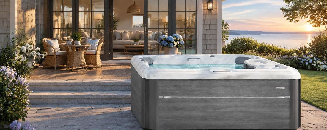 A wide-angle front view of a grey-paneled hot tub with a white marbled acrylic interior and waterfall feature