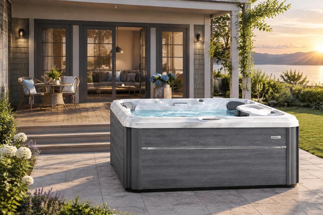 A wide-angle front view of a grey-paneled hot tub on a wooden deck with a marbled acrylic interior and waterfall feature
