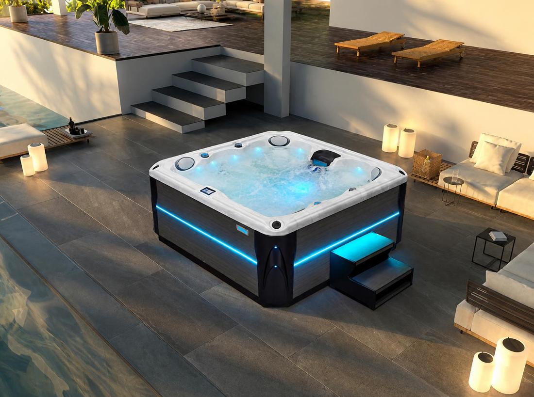 Wide-angle evening shot of hot tub illuminated with blue LED lighting on a stone patio