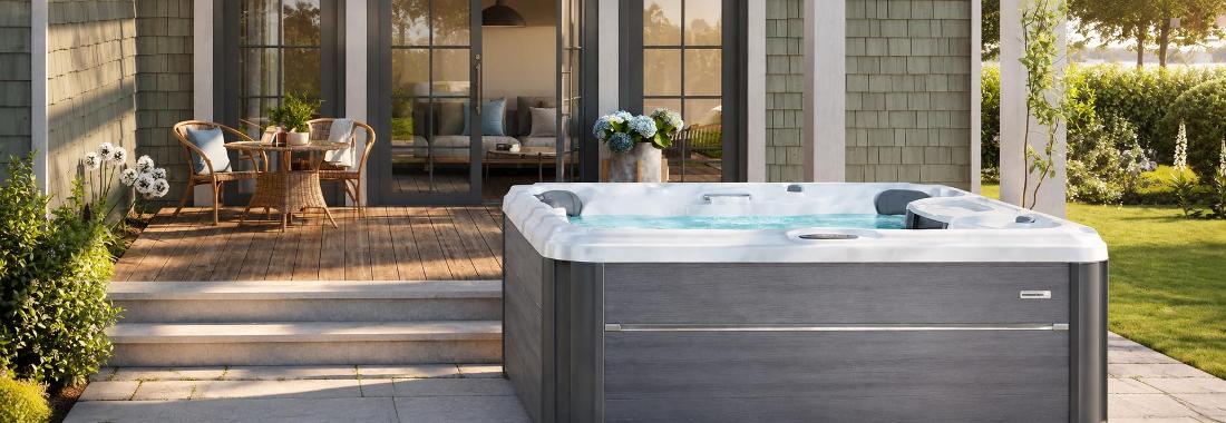 A wide-angle front view of a grey-paneled hot tub with waterfall feature on a wooden deck